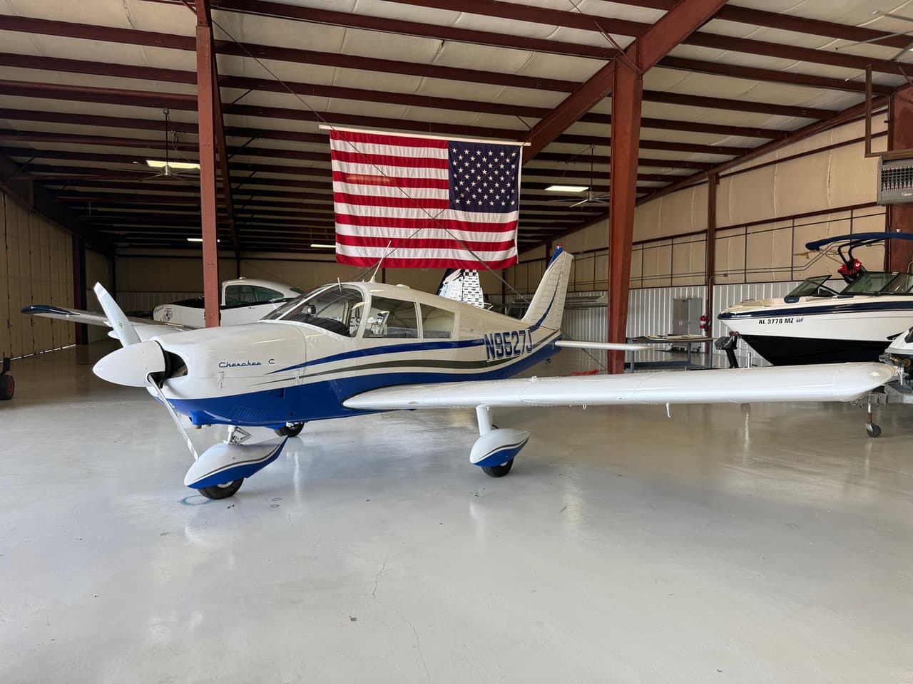 Oklahoma Flight Academy’s Piper Cherokee N9527J in the hangar beneath an American flag