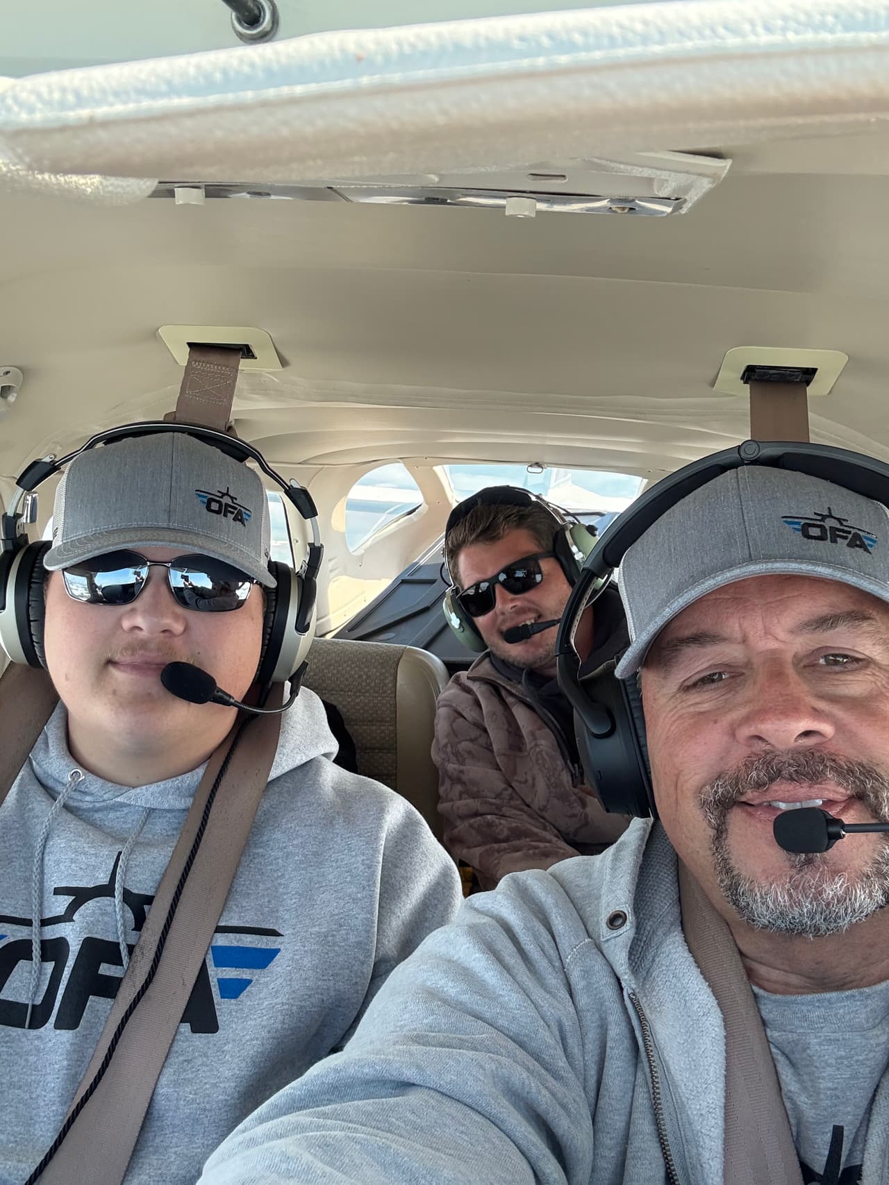 An Oklahoma Flight Academy instructor and students wearing OFA caps and aviation headsets in the cockpit during a training flight